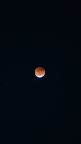 The image features a lunar eclipse with the moon appearing reddish against a dark night sky. Stars are faintly visible across the background.