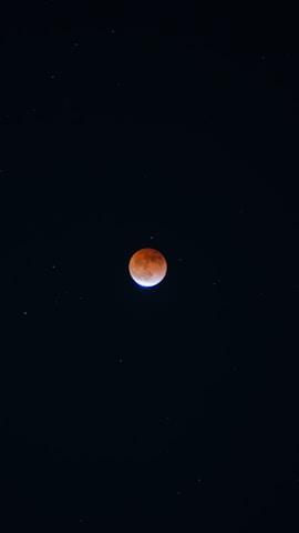 The image features a lunar eclipse with the moon appearing reddish against a dark night sky. Stars are faintly visible across the background.