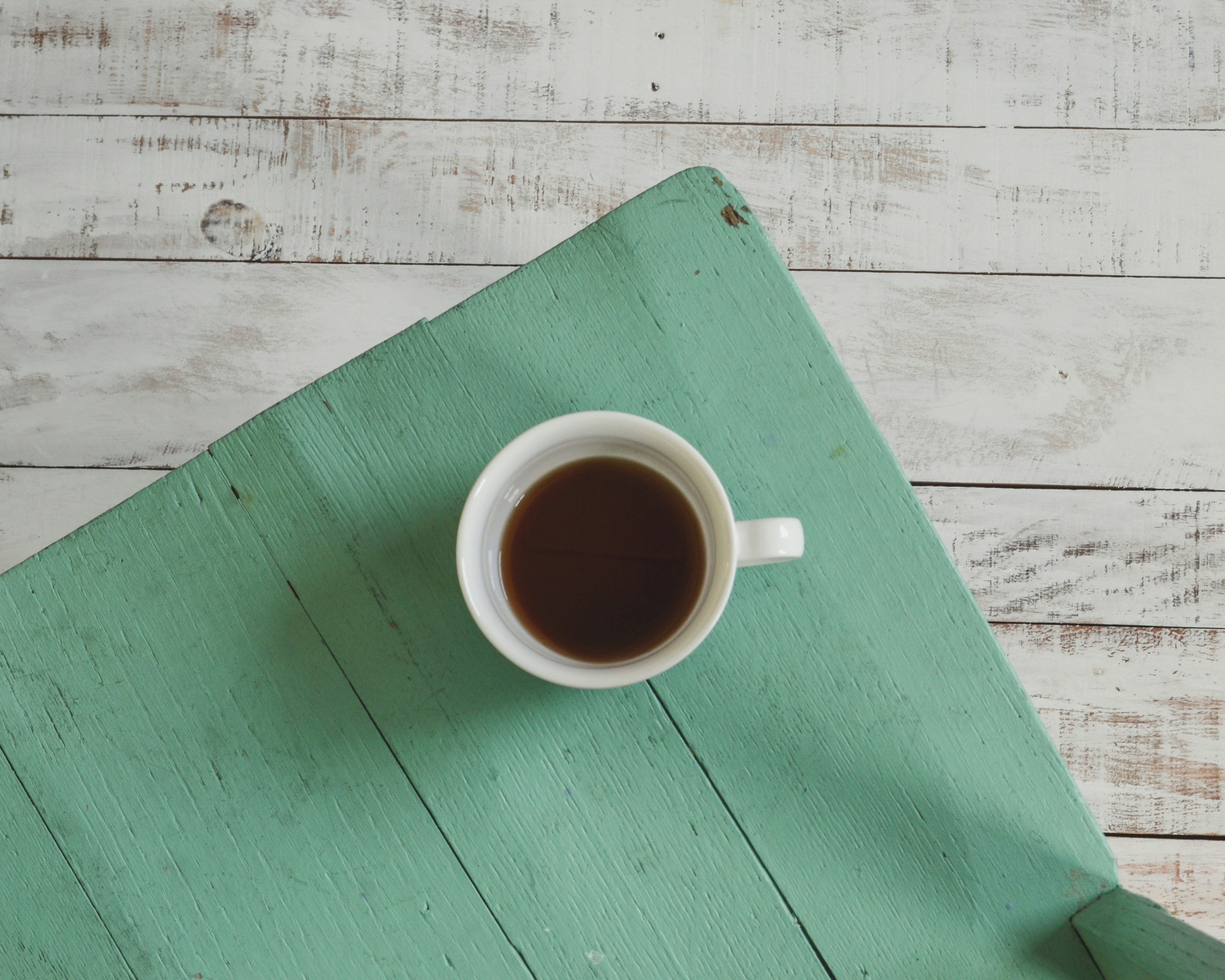 An overhead view of a coffee cup sitting on a wooden teal chair