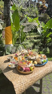 A person arranging traditional paper offerings on a wooden table outdoors.