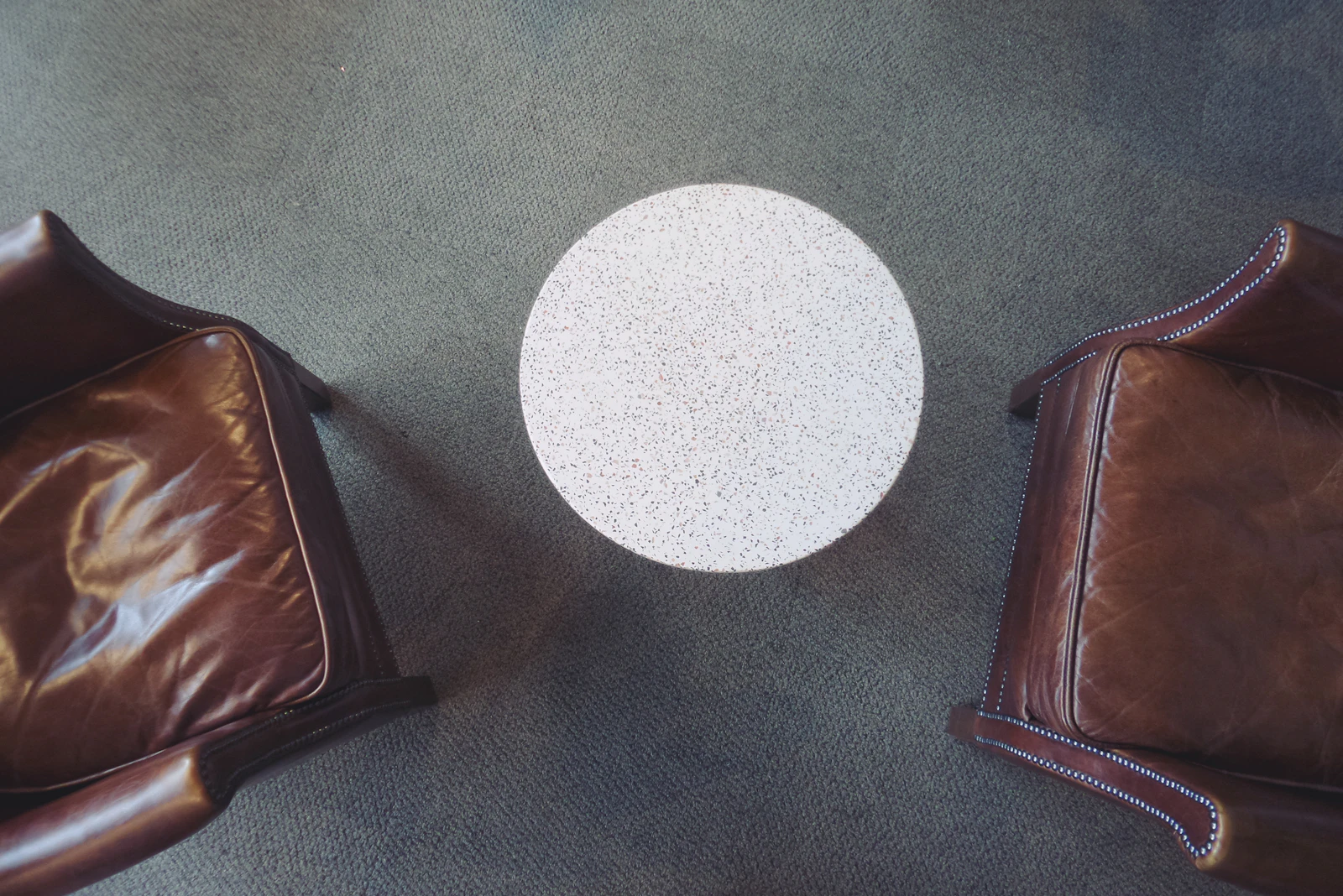 Two leather chairs and a round table on a carpet in the MANN studio