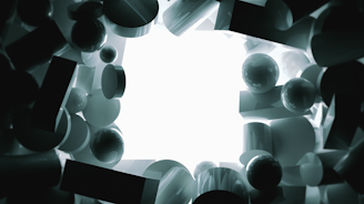 Various three-dimensional geometric shapes, including spheres, cylinders, and rectangles, are arranged with a bright white light source at the center. The shapes are dark in color and create a sense of depth and intrigue around the light.