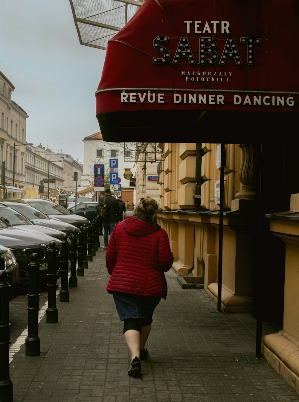 a woman in a red jacket walking down a sidewalk