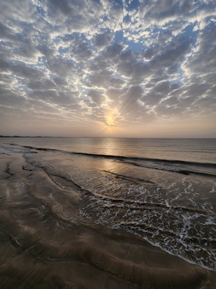 the sun is setting over the ocean on the beach