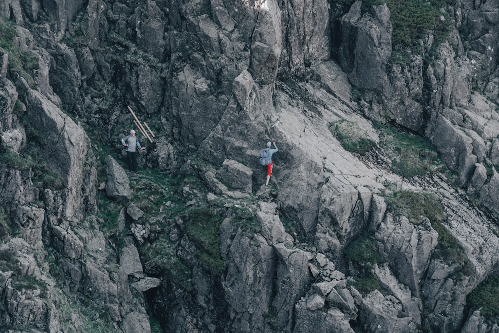 a couple of people climbing up the side of a mountain