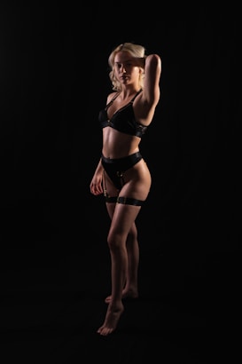 A female model poses confidently in minimal black clothing against a dark background, highlighting her features and form.