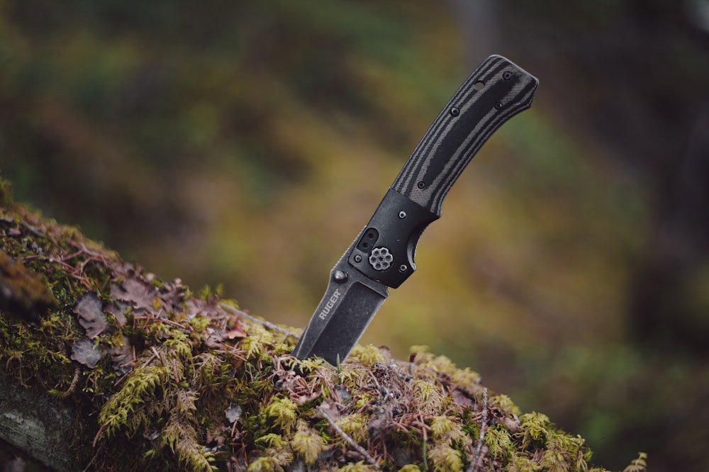 a black knife sitting on top of a moss covered tree