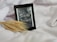 An e-reader displaying the cover of a book titled 'Sorcery of Thorns' by Margaret Rogerson rests on a soft, white fabric. A stalk of wheat is positioned beside the e-reader, adding a natural element to the scene. The color scheme of the e-book cover is primarily grayscale.