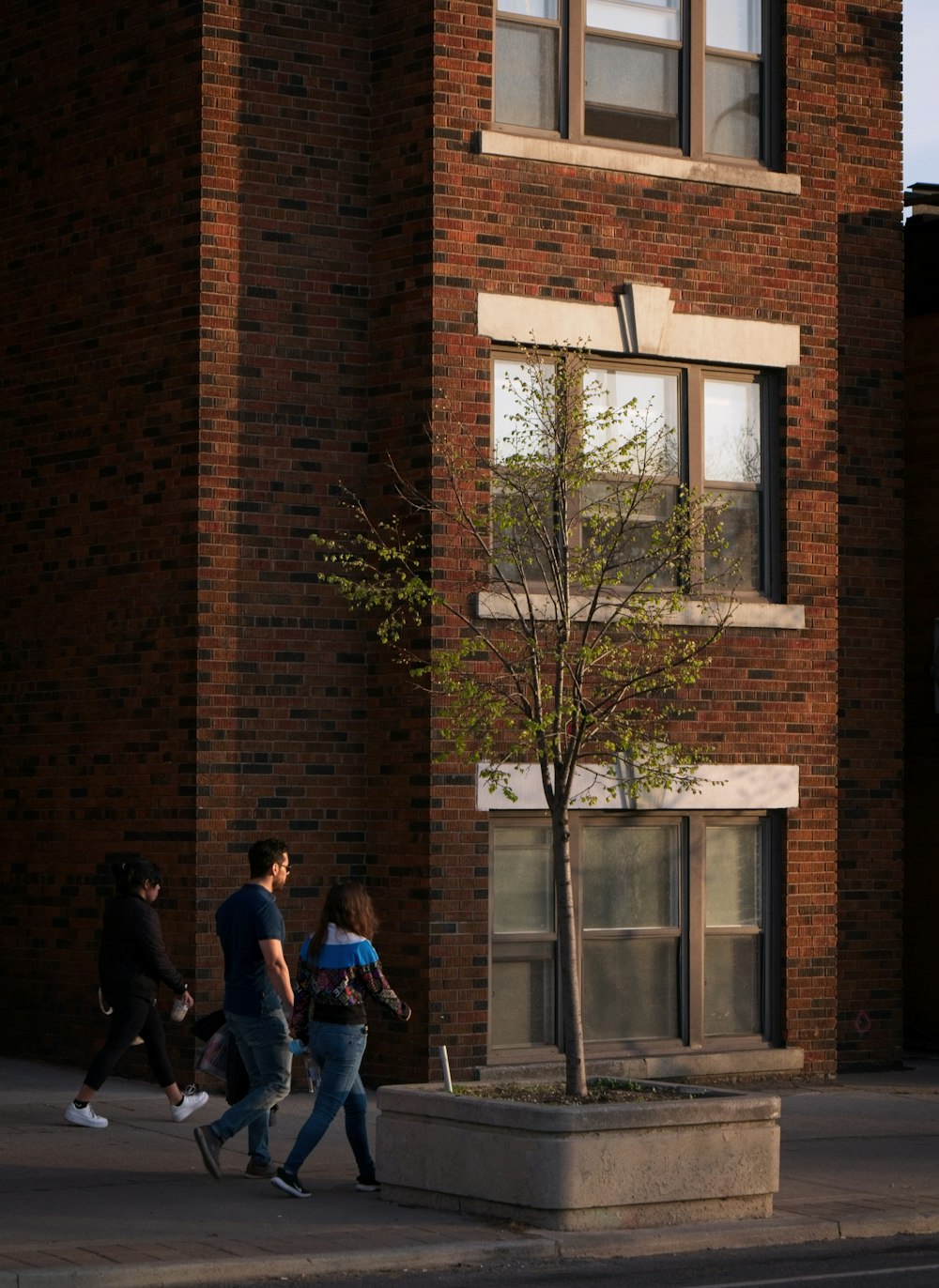 a group of people walking past a tall brick building
