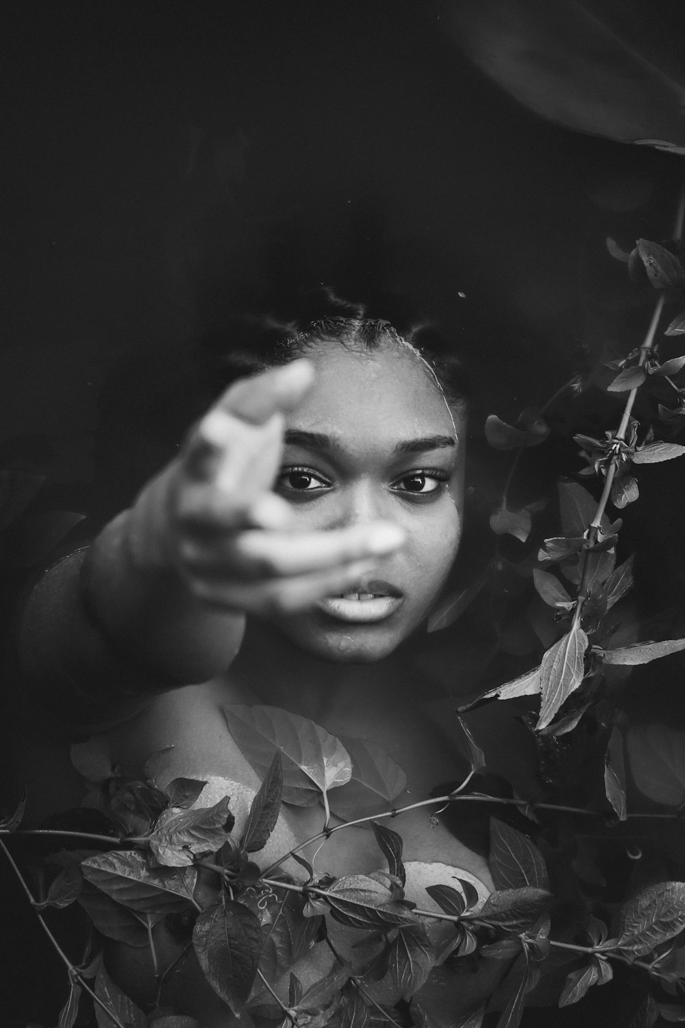 a black and white photo of a woman peeking out from behind a bush
