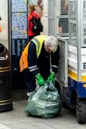 a man in a yellow safety vest and green gloves unloads a garbage bag