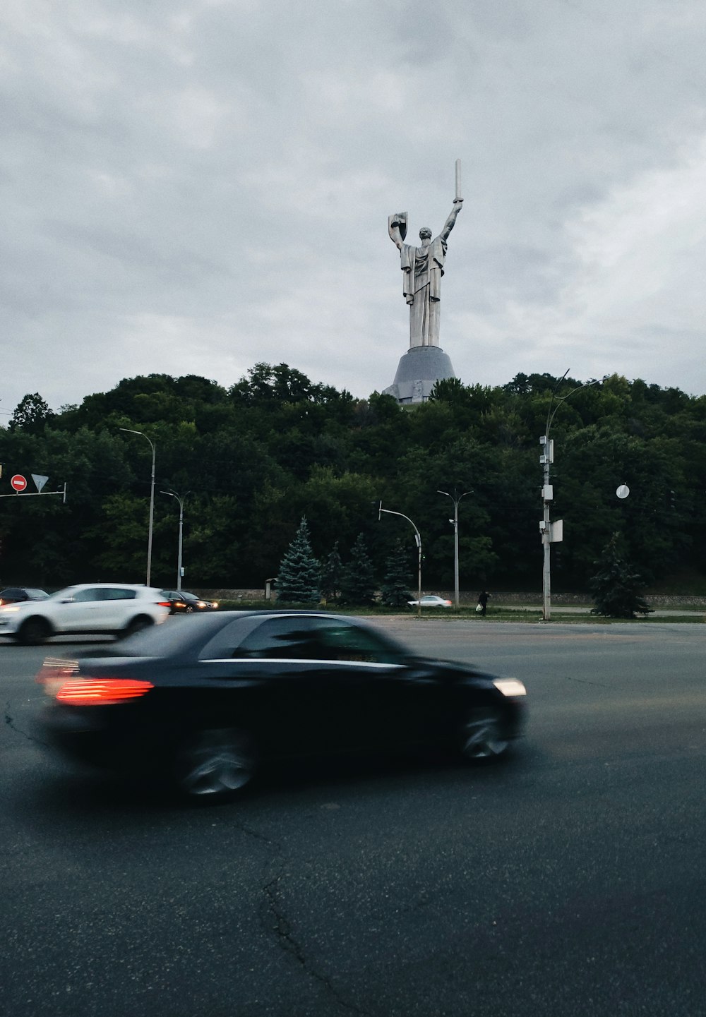 a car driving past a statue on a cloudy day