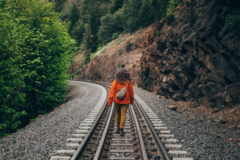 a woman walking on train tracks in the woods