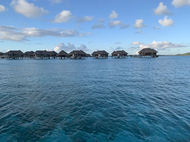 Overwater bungalows stretching into the calm blue sea under a bright sunny sky.