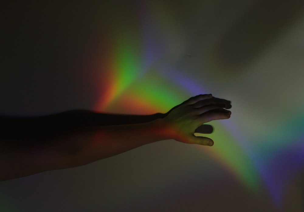 a person's hand with a rainbow light in the background