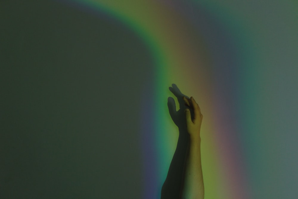 a person's hand reaching up to a rainbow