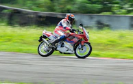 Action shot of a racer wearing Hyper Flow Racing gear speeding on a track, blurred background emphasizing motion.