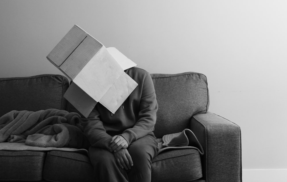Eine Person, die mit einem Buch auf dem Kopf auf einer Couch sitzt