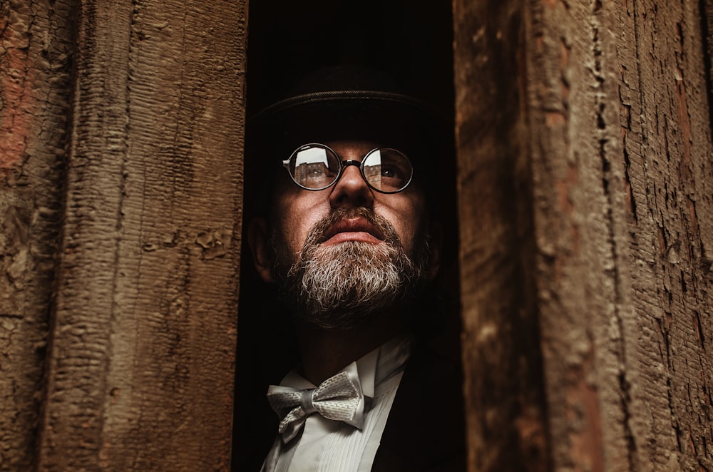 a man with a hat and glasses looking out of a hole