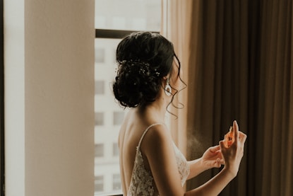 a woman standing in front of a window spraying perfume