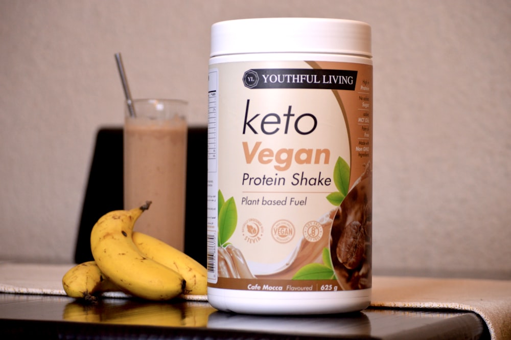 Una botella de keto vegan junto a un plátano y un vaso de chocolate