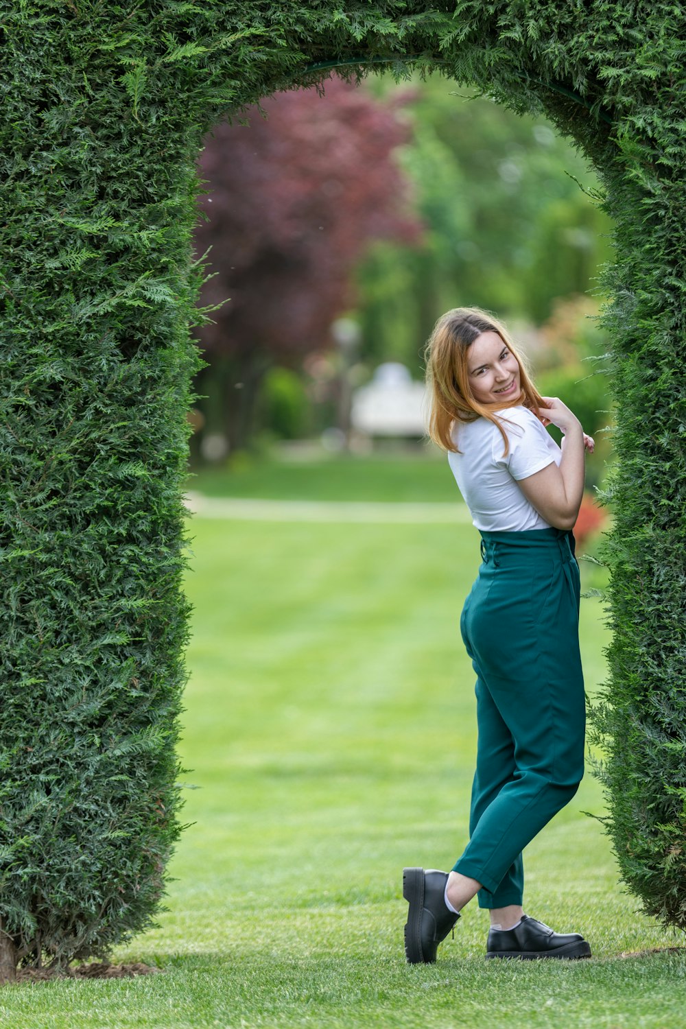 a woman standing in front of a green hedge