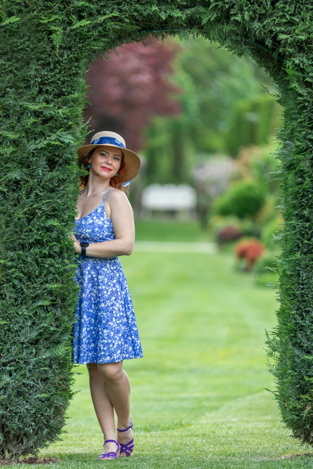 a woman in a blue dress and hat standing in a garden