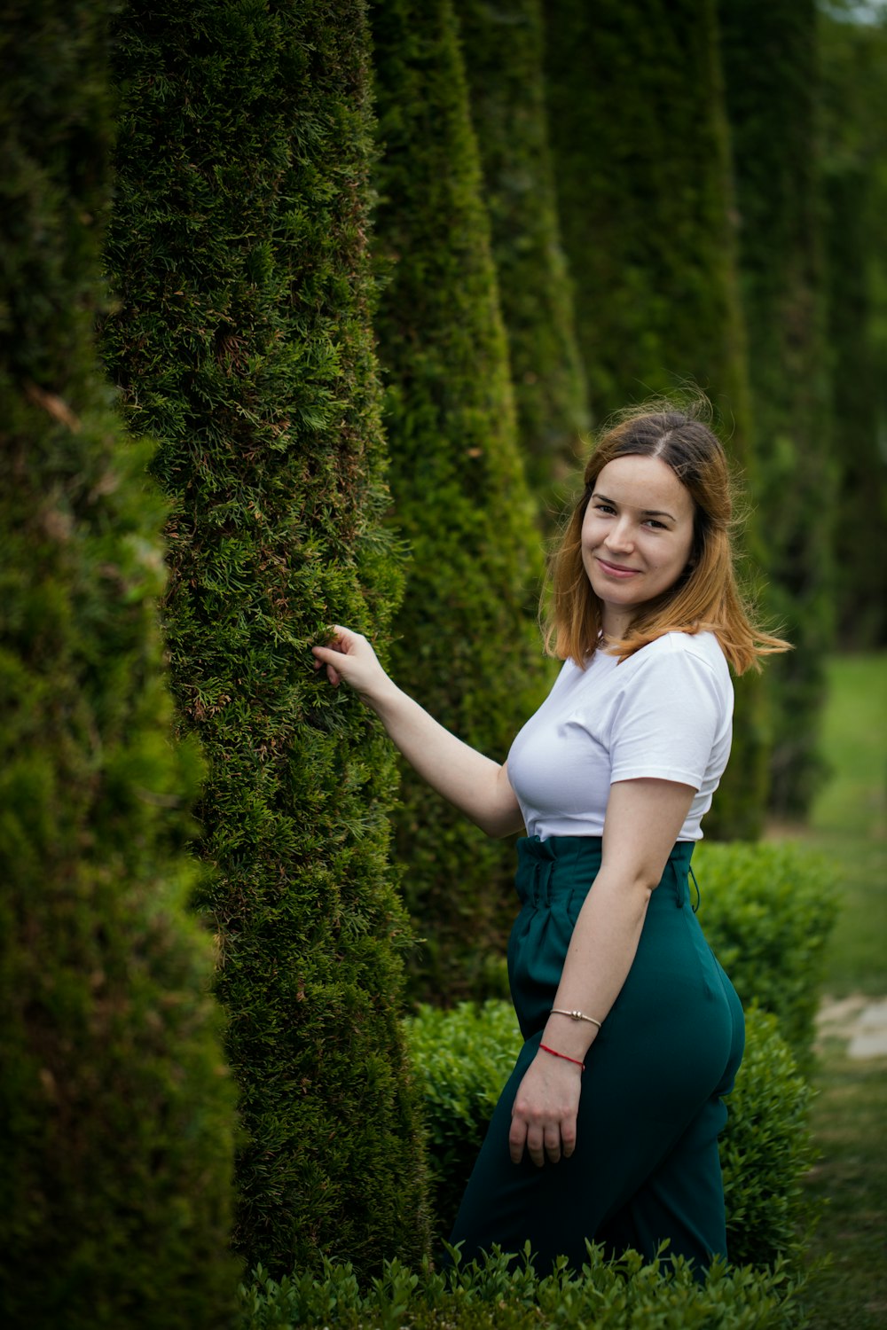 a woman standing between two tall green trees