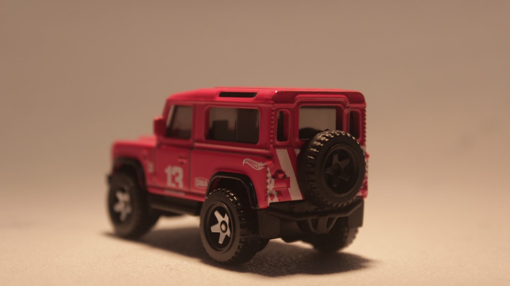 a red toy jeep is on a white surface