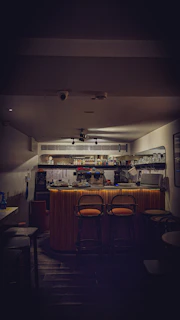 A sleek, dimly lit bar counter with polished wood and softly glowing amber lights reflecting off crystal glassware.