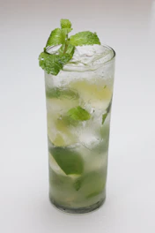A sparkling mojito drink garnished with fresh mint leaves and lime wedges in a clear glass.