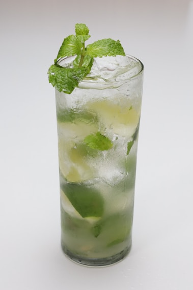 A vibrant cocktail with fresh lime and mint leaves, glowing under colorful club lights.