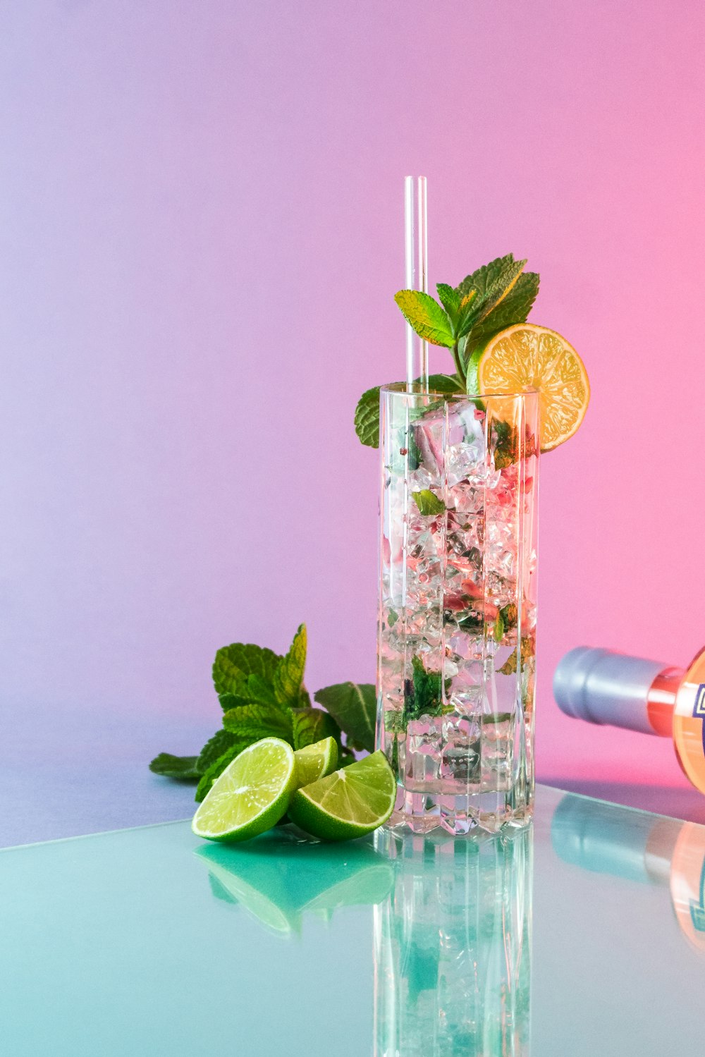 a glass filled with ice and limes next to a bottle of vodka