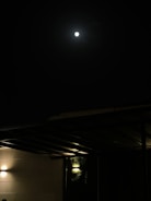 A night sky with a bright full moon shining over a quiet chapel roof.