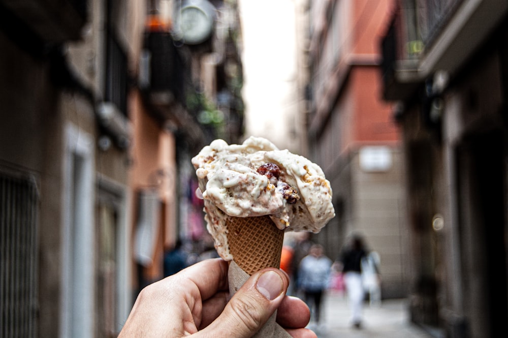 a hand holding an ice cream cone on a city street