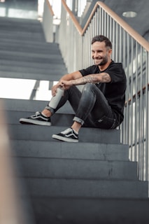 Man sitting on stairs wearing a printed t-shirt and casual shoes, smiling
