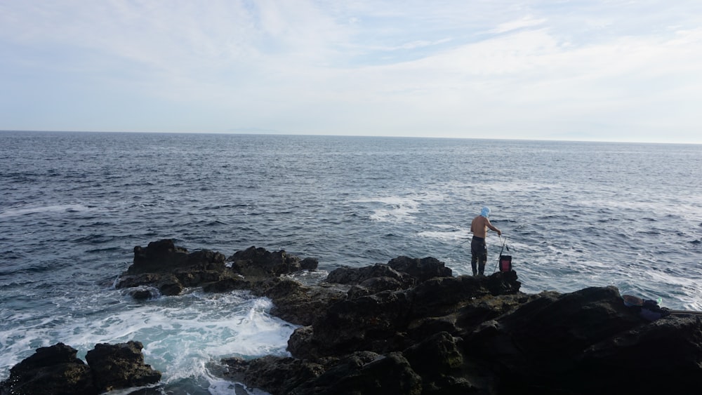 a man standing on top of a rocky cliff next to the ocean