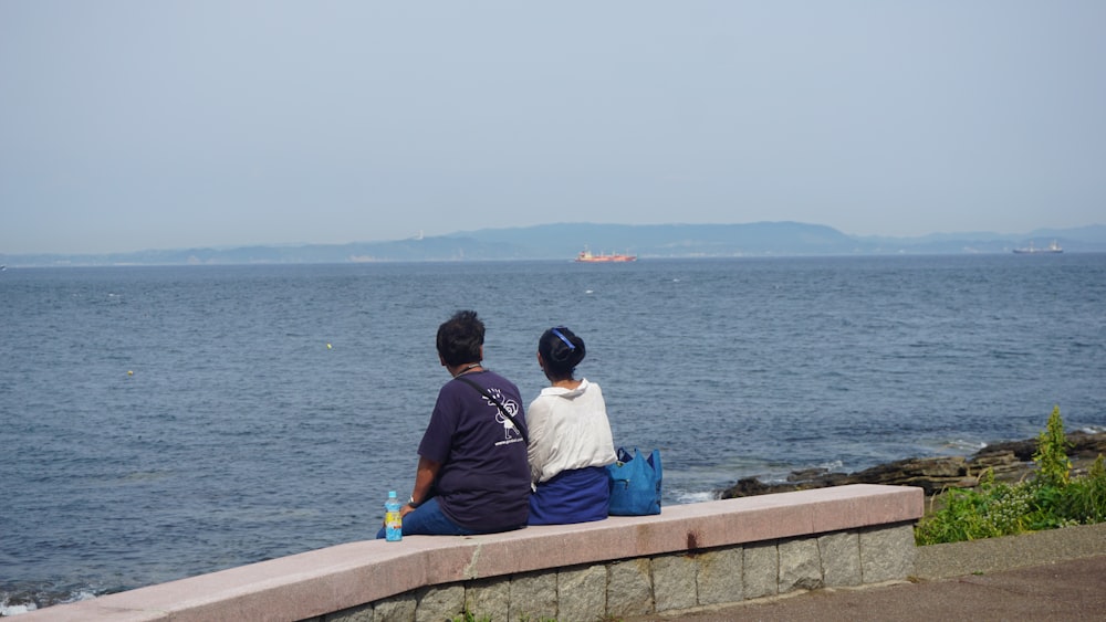 a couple of people sitting on top of a stone wall