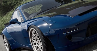 A sleek, modified sports car with a shiny blue exterior and white rims is parked or moving slowly on an asphalt road. The car features a carbon fiber hood and a distinct aerodynamic design, complemented by lush green foliage in the background that contrasts with the car's polished surface.