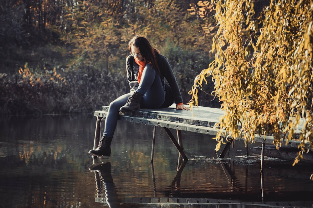 a woman sitting on a bench next to a body of water