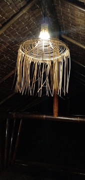 A hanging lamp made from alang-alang thatch casting warm, inviting light over a wooden dining area.