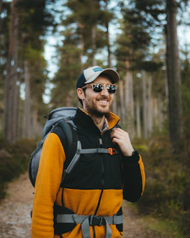 A cheerful dad with a backpack thumb-hiking along a sunny country road.
