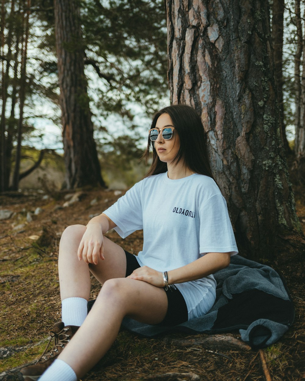 a woman sitting on the ground next to a tree