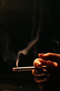 Close-up of a hand holding a cigarette with smoke curling upwards.