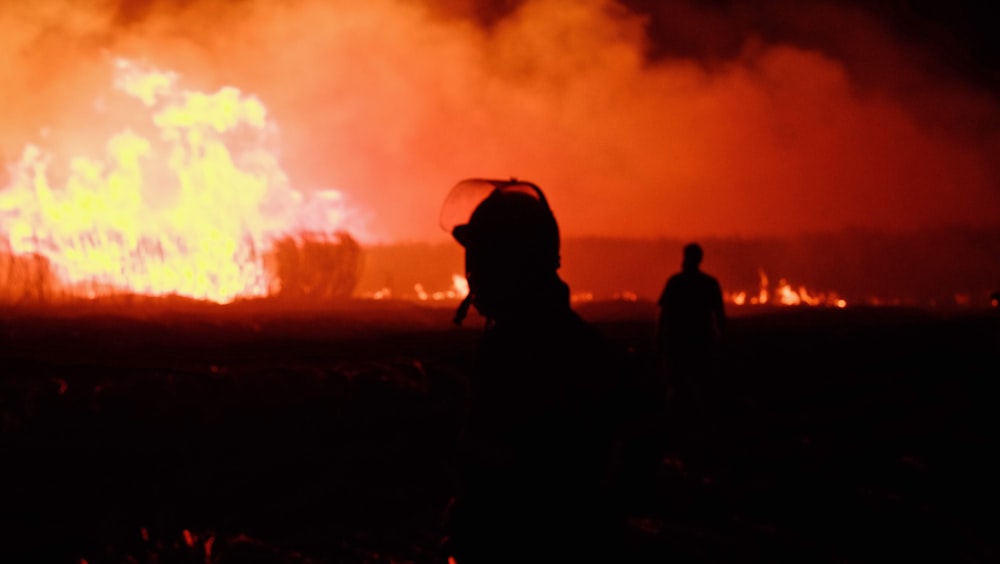 two people standing in front of a large fire