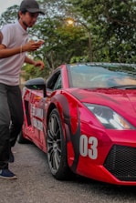A person in a white shirt and cap appears to be moving past a red sports car with the number 03 on its front. The car has visible rain droplets and is set against a backdrop of trees. The words 'Sri Lanka Run 2019' are also visible on the side of the car.