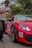 A person in a white shirt and cap appears to be moving past a red sports car with the number 03 on its front. The car has visible rain droplets and is set against a backdrop of trees. The words 'Sri Lanka Run 2019' are also visible on the side of the car.
