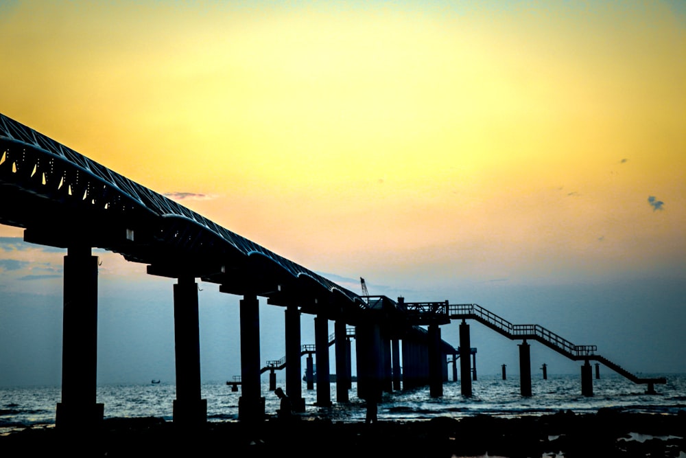 the sun is setting over the ocean with a pier in the foreground