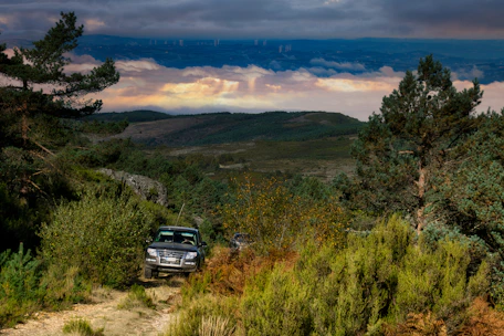 A rugged vehicle driving through a rural mountain path surrounded by lush greenery.
