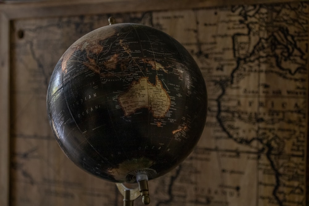 Un globo terráqueo negro y dorado en un soporte frente a un mapa